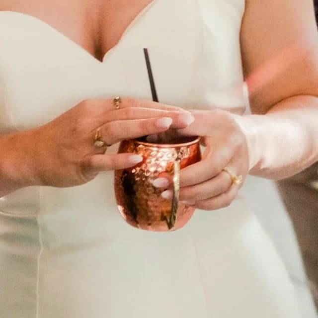 The bride's hands and rings around a hammered copper mug, at full size