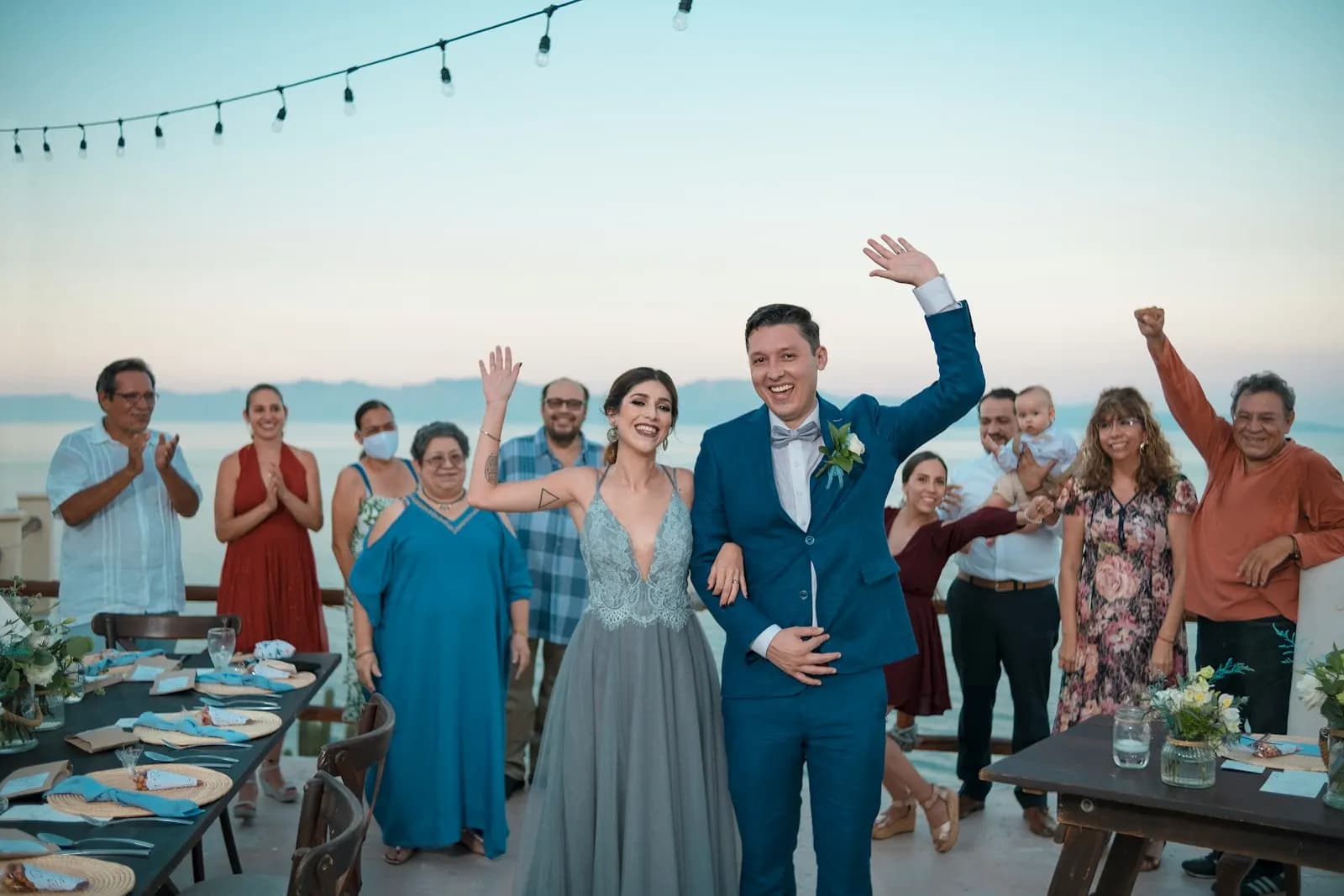 The bride, the groom and their guests cheering by the sea at golden hour