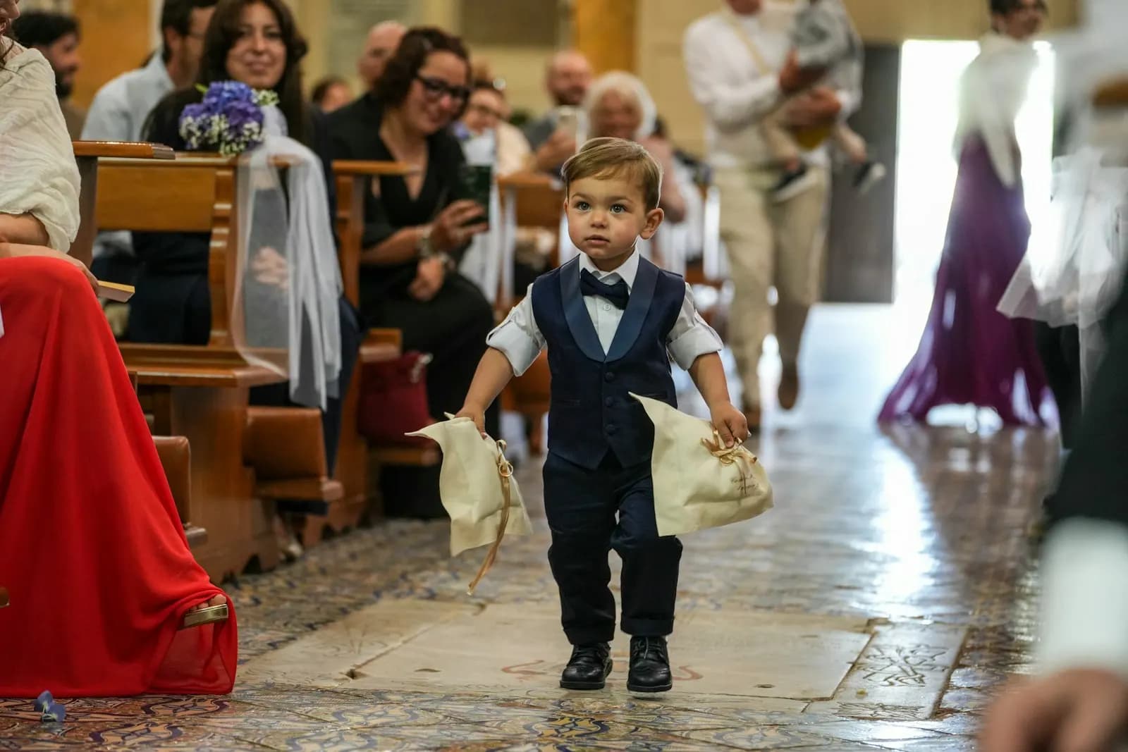 A small boy in a waistcoat walking down the aisle