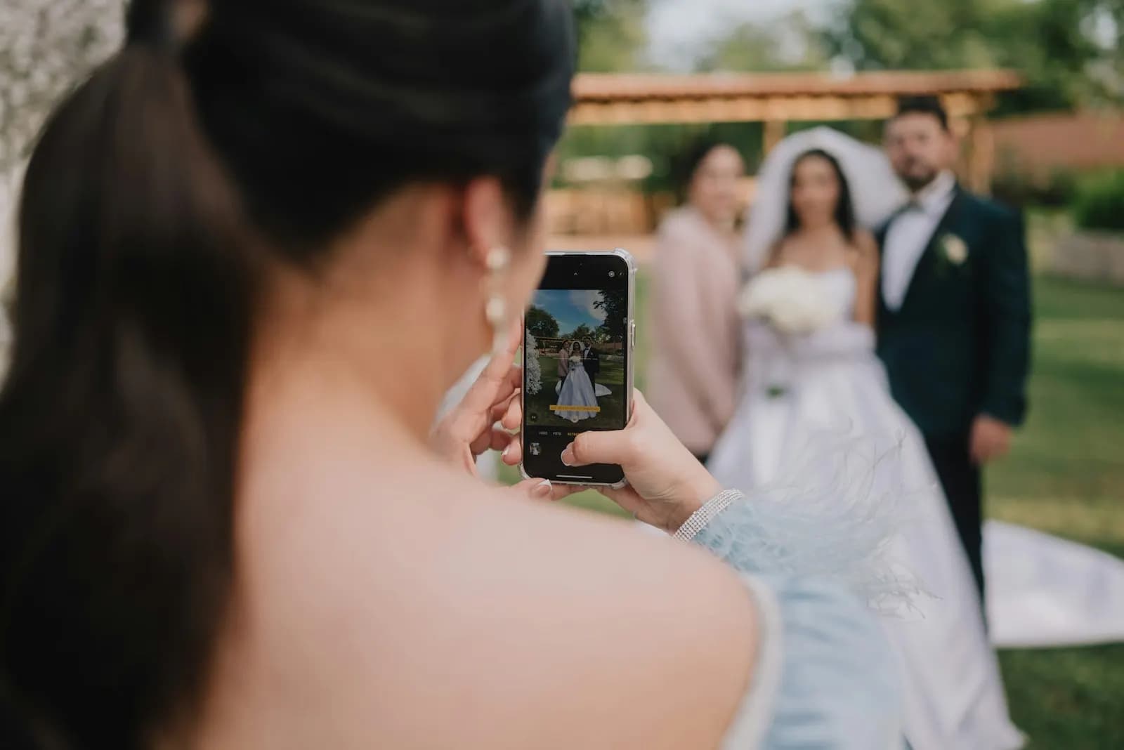 A wedding guest photographs the bride and groom on her phone