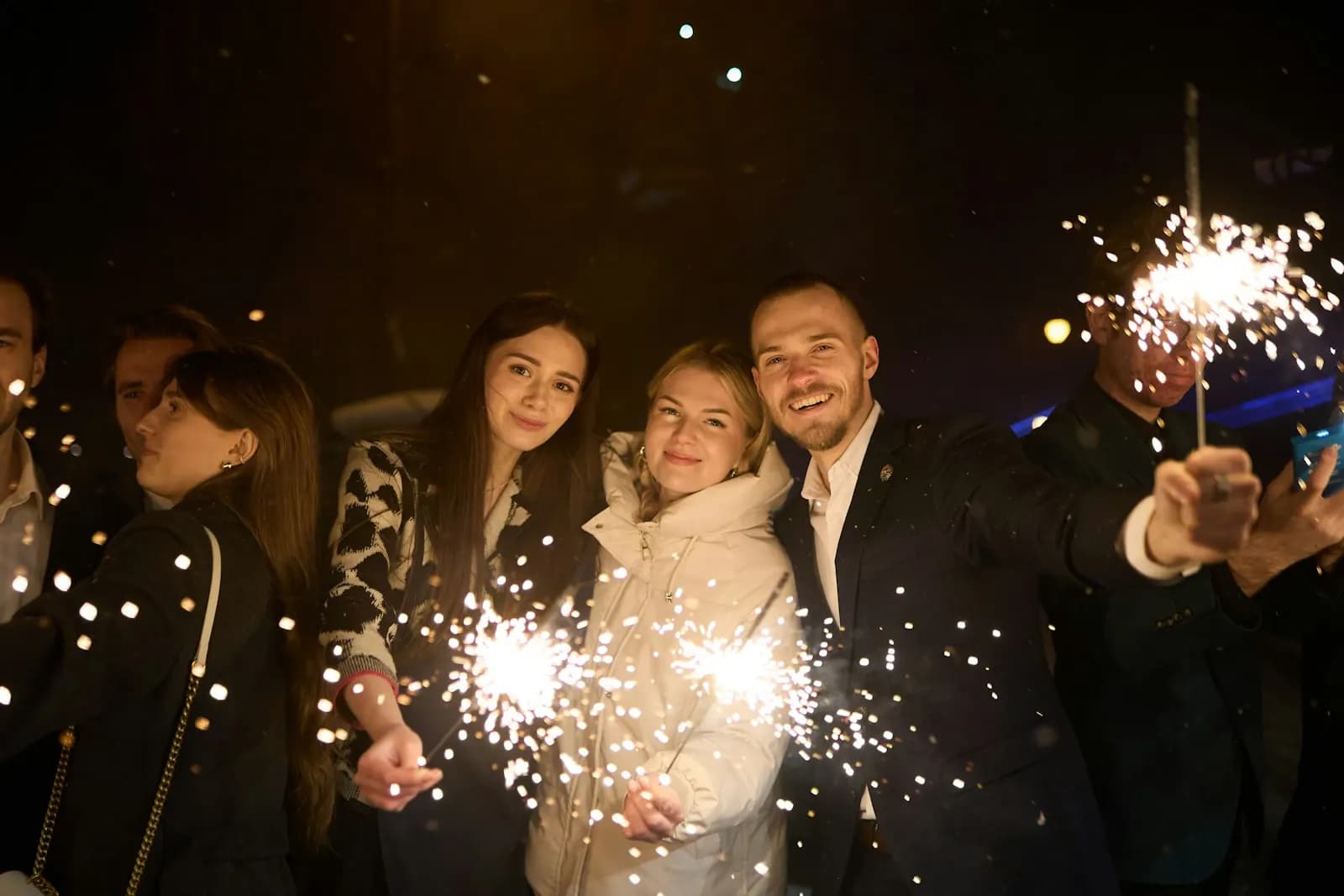 Friends holding sparklers at night, grinning
