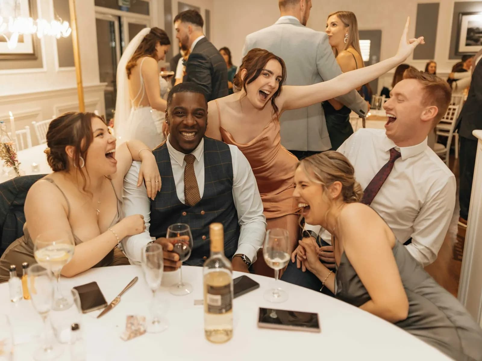 Friends laughing around a white reception table with wine glasses