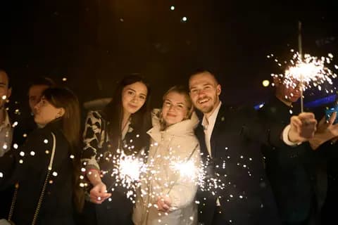 Friends holding sparklers at night, grinning