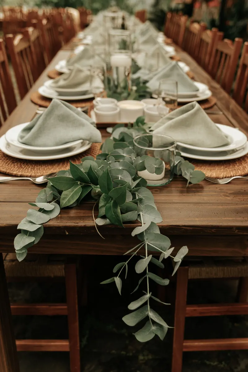 Eucalyptus garland running down a wooden wedding table between plates, napkins and glass candle holders
