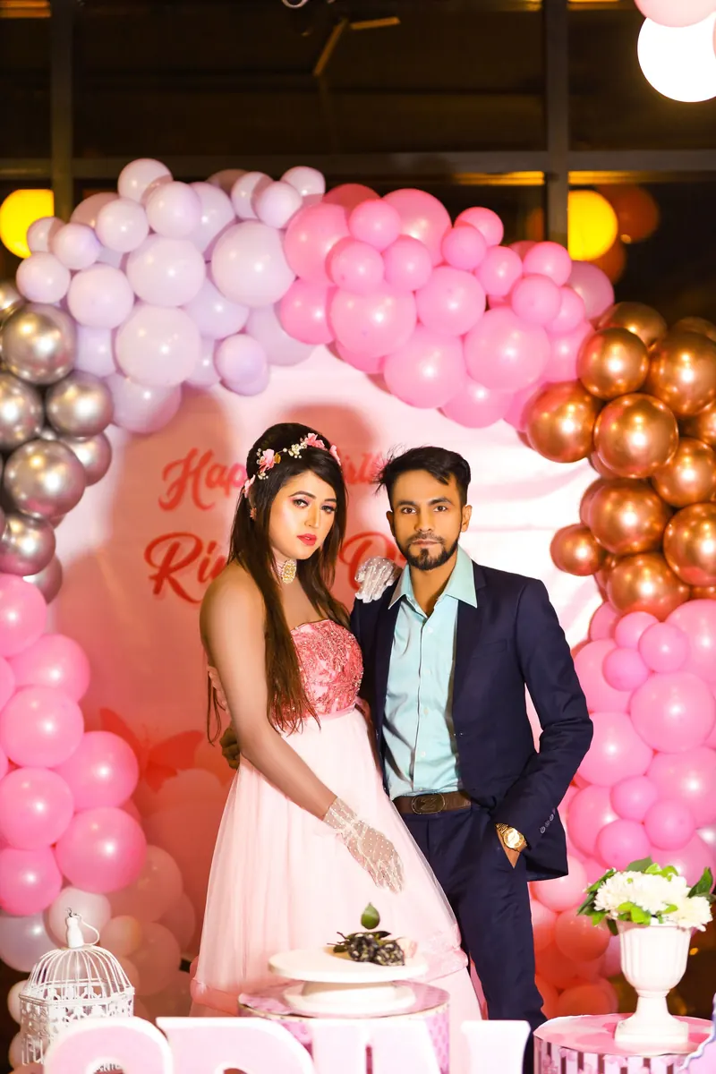 Bride and groom standing in front of a wall of pink, white and gold balloons at their wedding