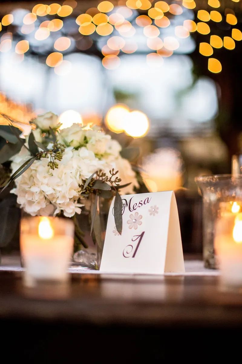 Wedding table at night with white flowers, glowing candles in glass holders and a table number card