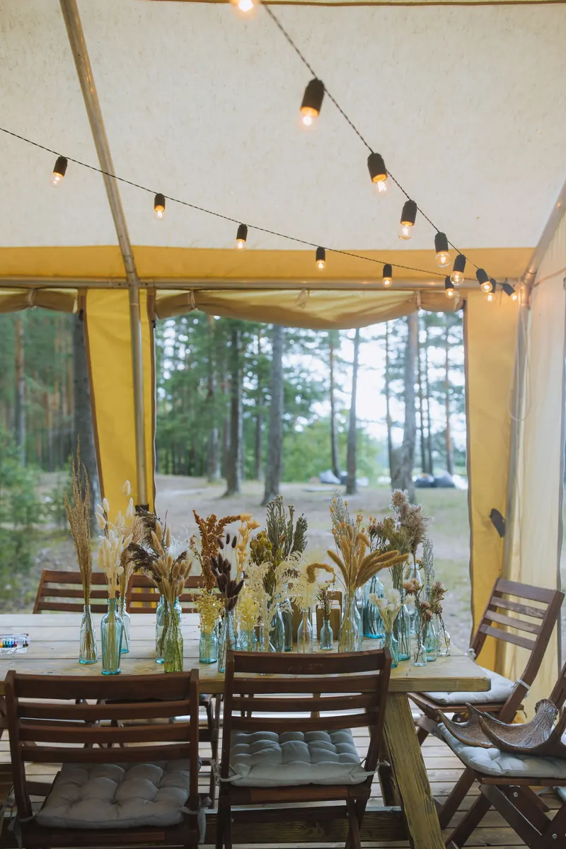Wedding dining table inside a white marquee tent with festoon string lights overhead and flower centerpieces