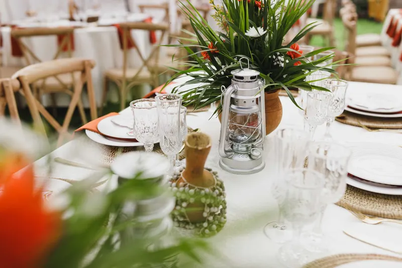 Table set with white cloth and glassware, a metal lantern and a tropical floral centerpiece