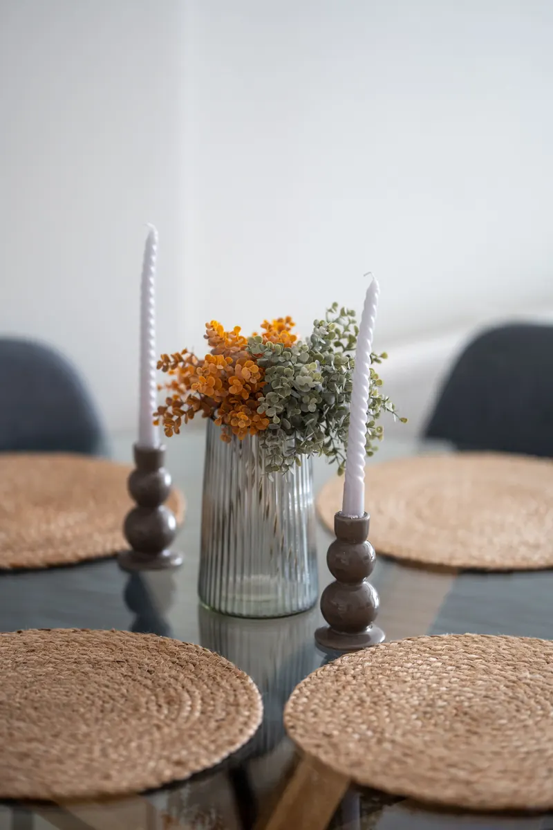 Minimal table with a single vase of orange flowers, two white taper candles and woven placemats