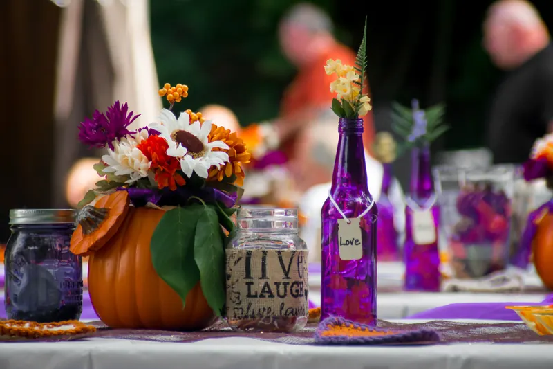 Wedding table decorated with a pumpkin vase of autumn flowers, purple bottles and jars