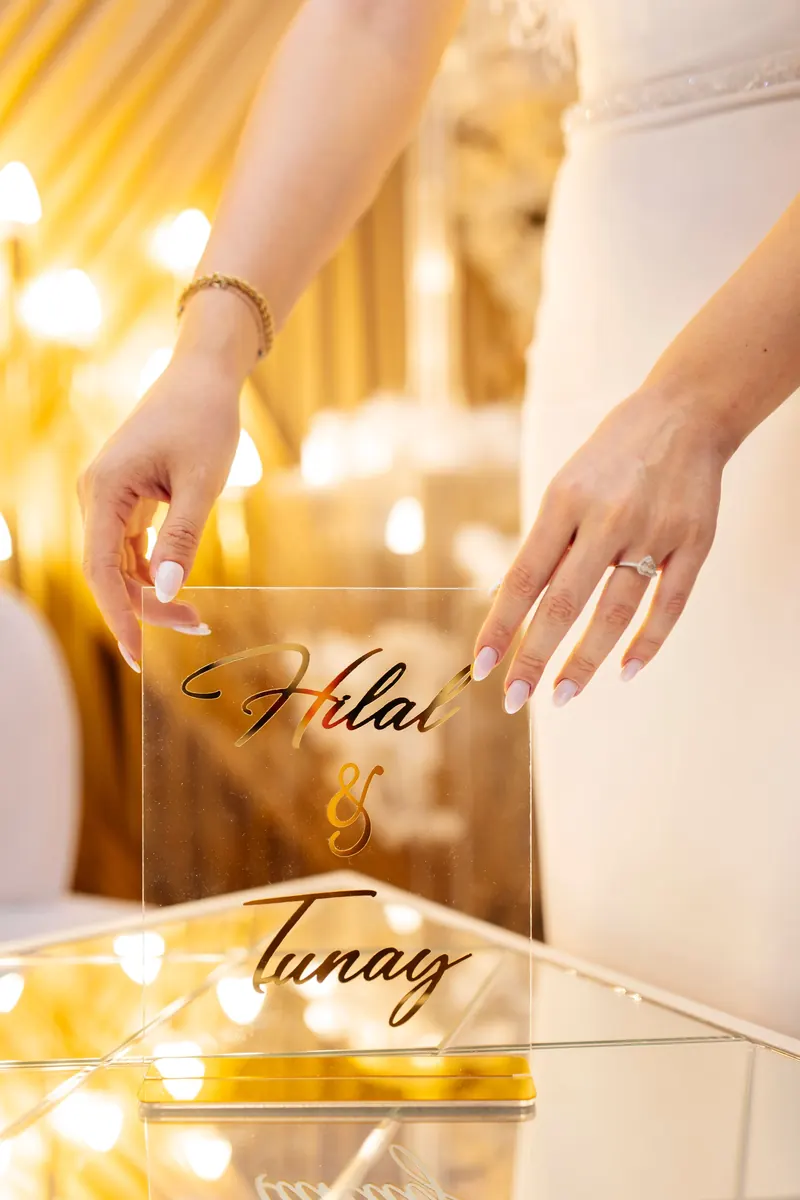 Bride's hands holding a clear acrylic wedding sign with names in gold lettering in warm light