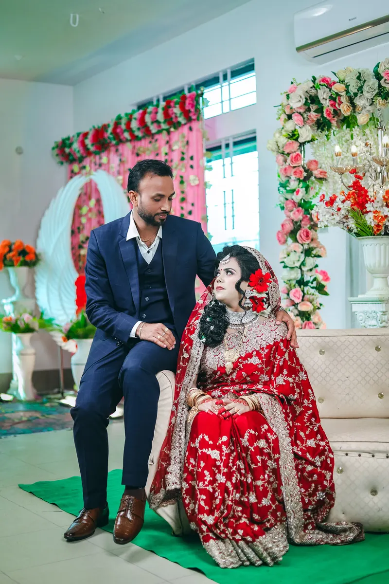 Bride and groom on a cream tufted sofa in front of floral garlands at their wedding reception