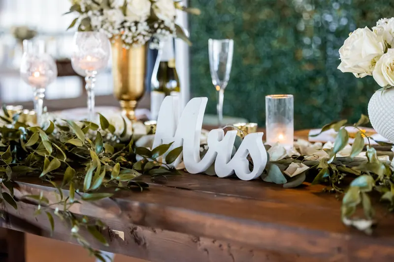 Freestanding white Mrs letters on a wooden wedding table with greenery garland, white flowers and candles