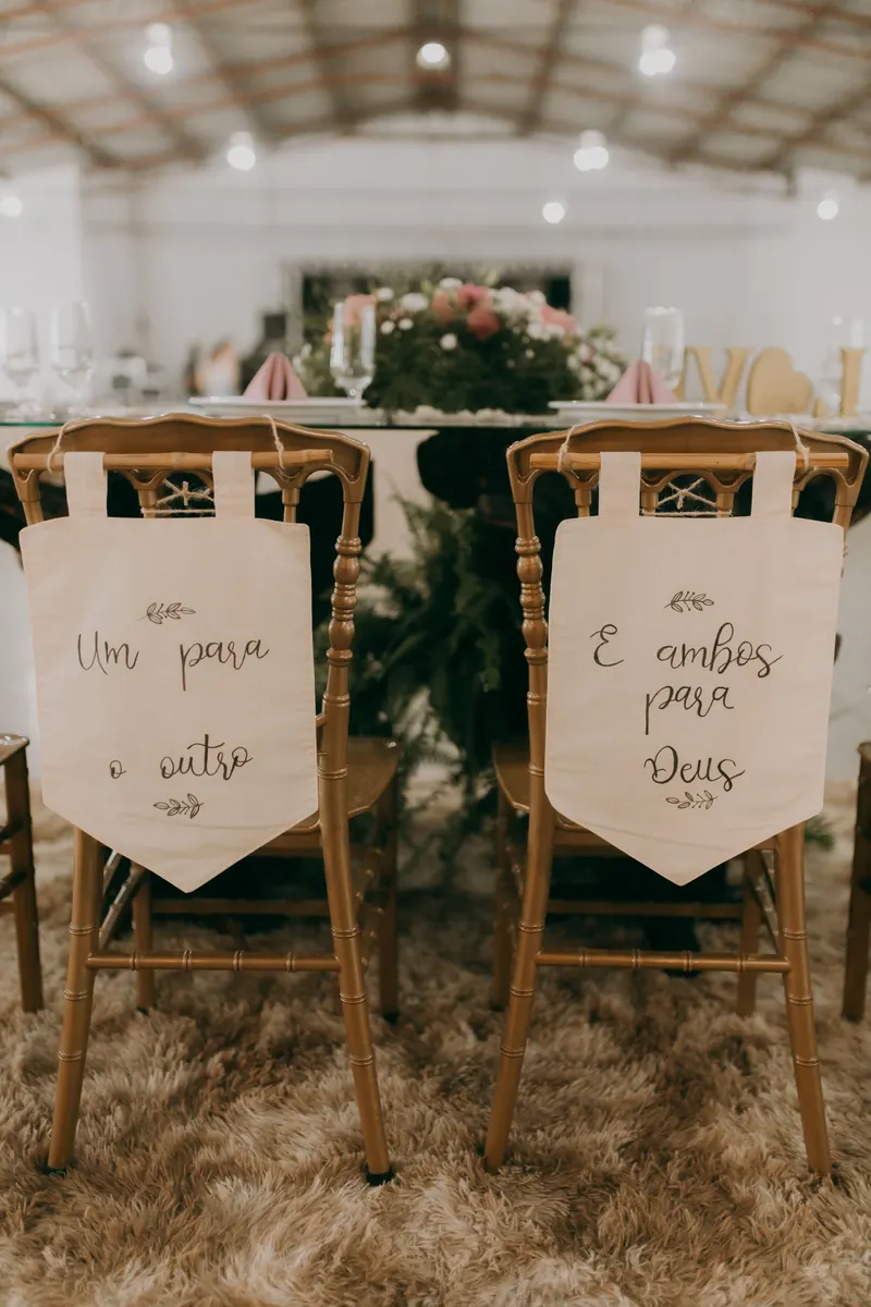 Two wooden chairs with hand-lettered fabric banners tied to their backs at a wedding reception