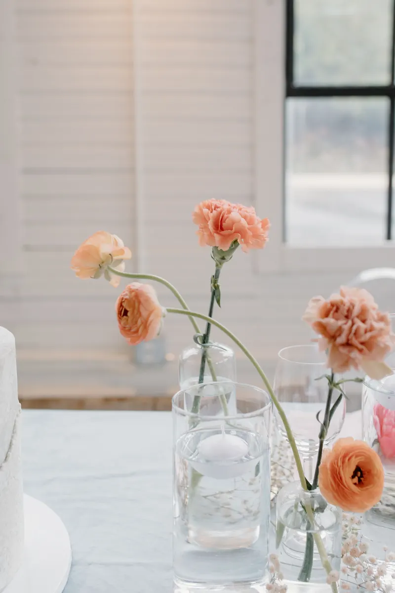 Clear glass bud vases holding single pink and peach flowers on a white table